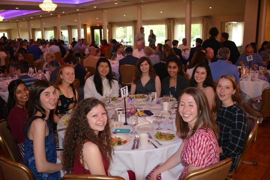 A group of young women are sitting at a table in a large room.