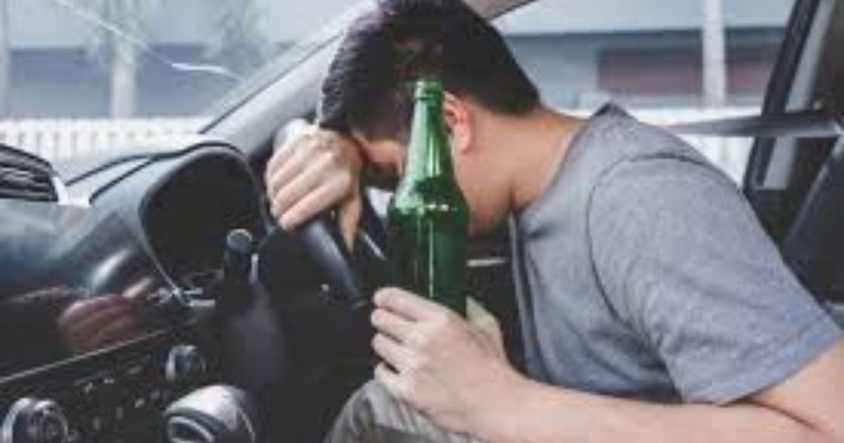 Man slumped over steering wheel, holding beer bottle in car.
