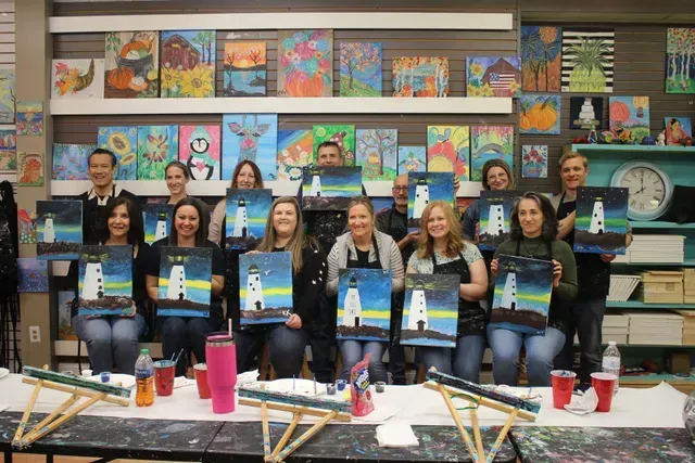 A group of people are sitting at a table holding paintings.