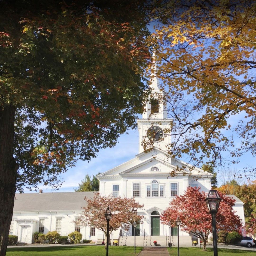 A white church with a clock tower is surrounded by trees