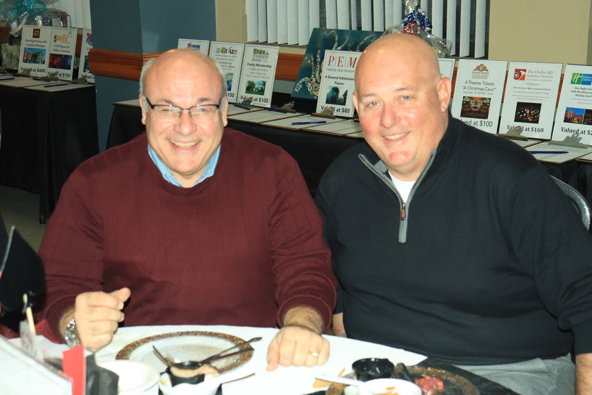 Two men are sitting at a table and one of them is wearing a red sweater