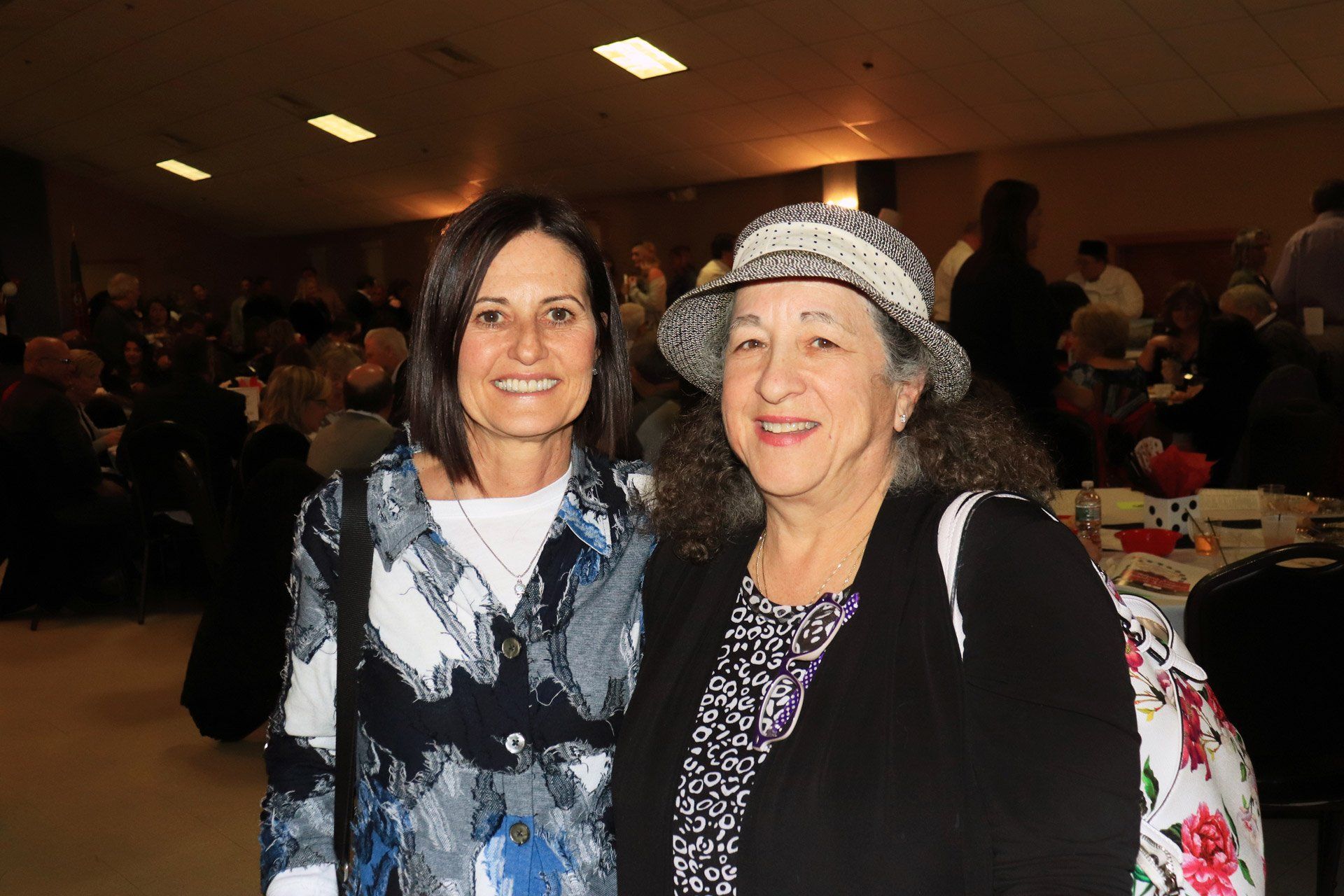 Two women are posing for a picture together in a room . one of the women is wearing a hat.