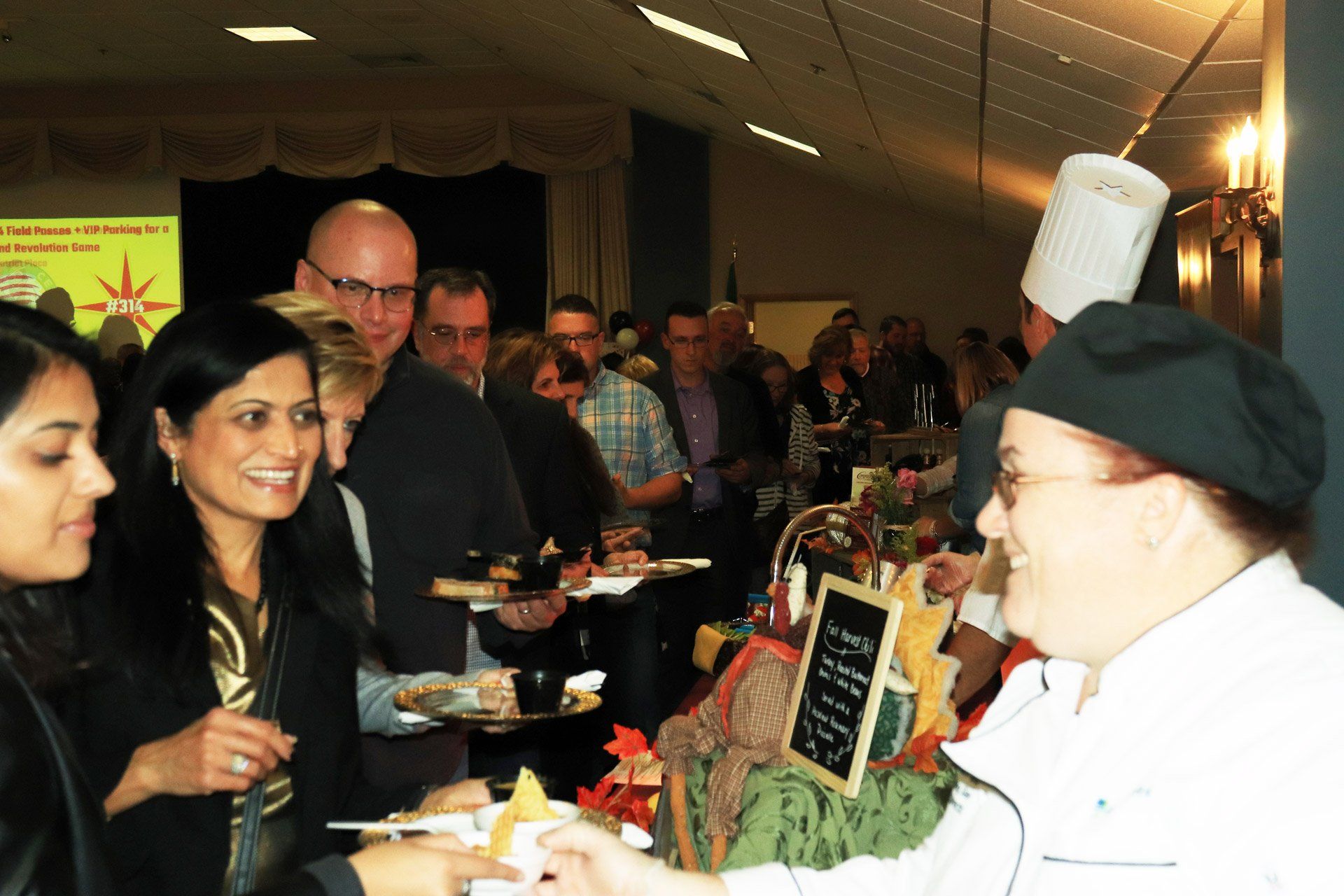 A woman in a chef 's hat is serving food to a group of people