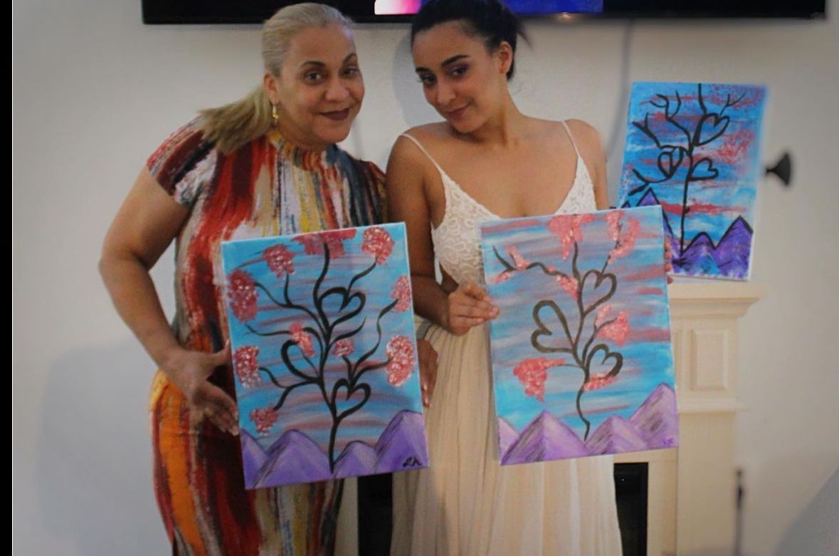 Two women are standing next to each other holding paintings.