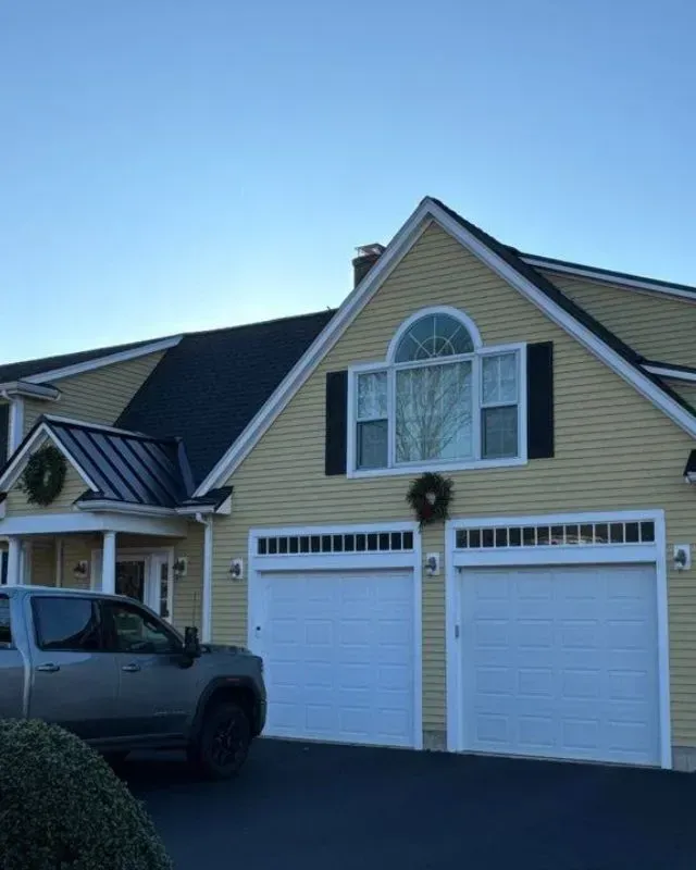 A car is parked in front of a house with two garage doors