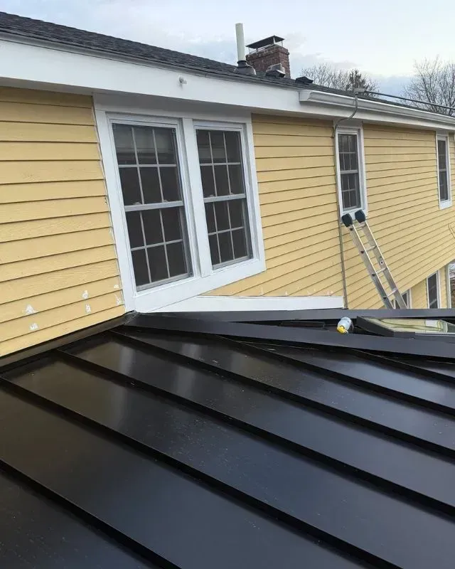 A yellow house with a black roof and windows