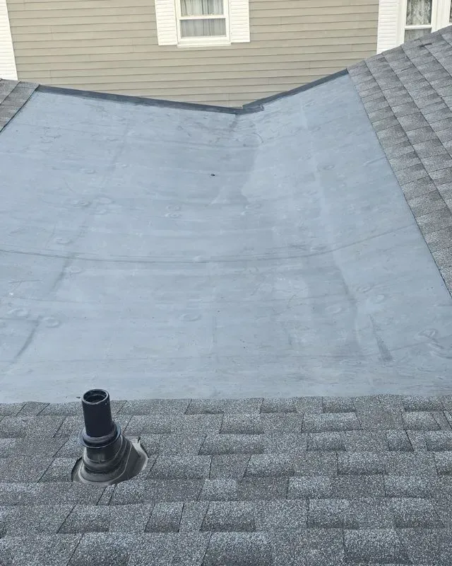A roof with a chimney on it and a house in the background.