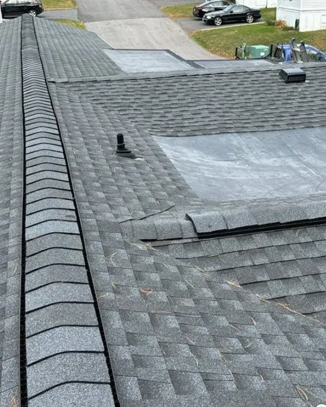 A close up of a roof with shingles and a drain on it.