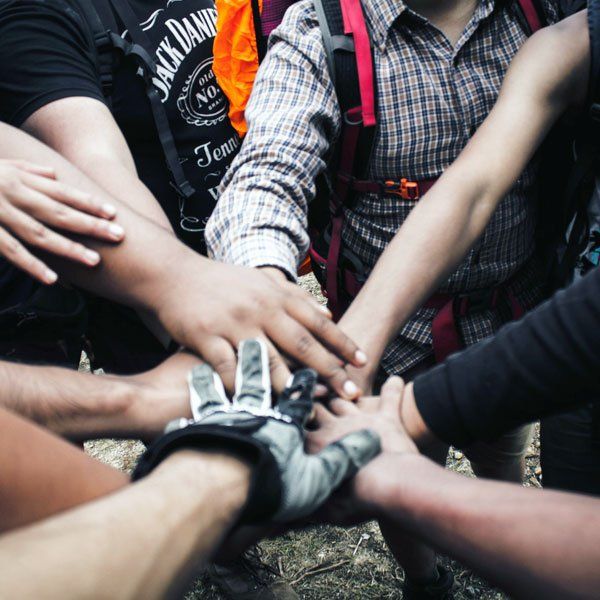 Group of people with hands together, emphasizing teamwork. One person wears a glove.
