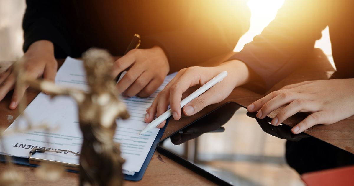 Two people signing legal documents at a table; Lady Justice statue in the foreground.
