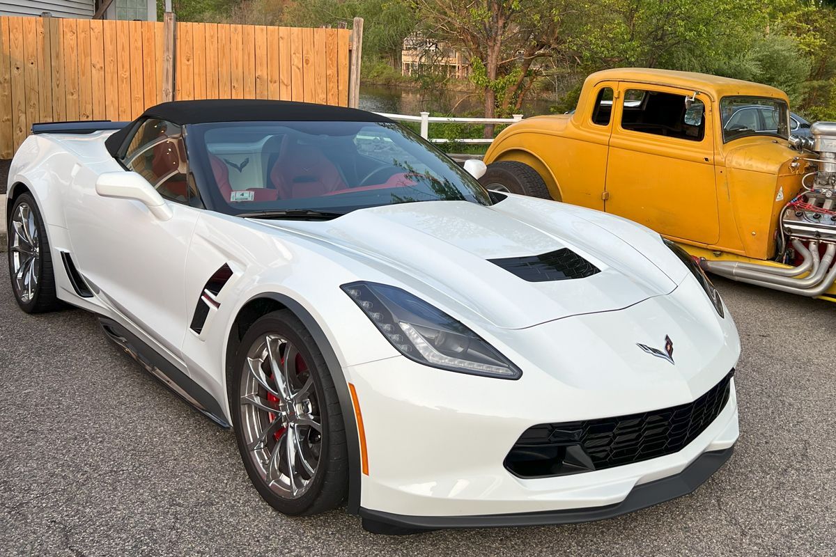 A white corvette convertible is parked next to a yellow hot rod.