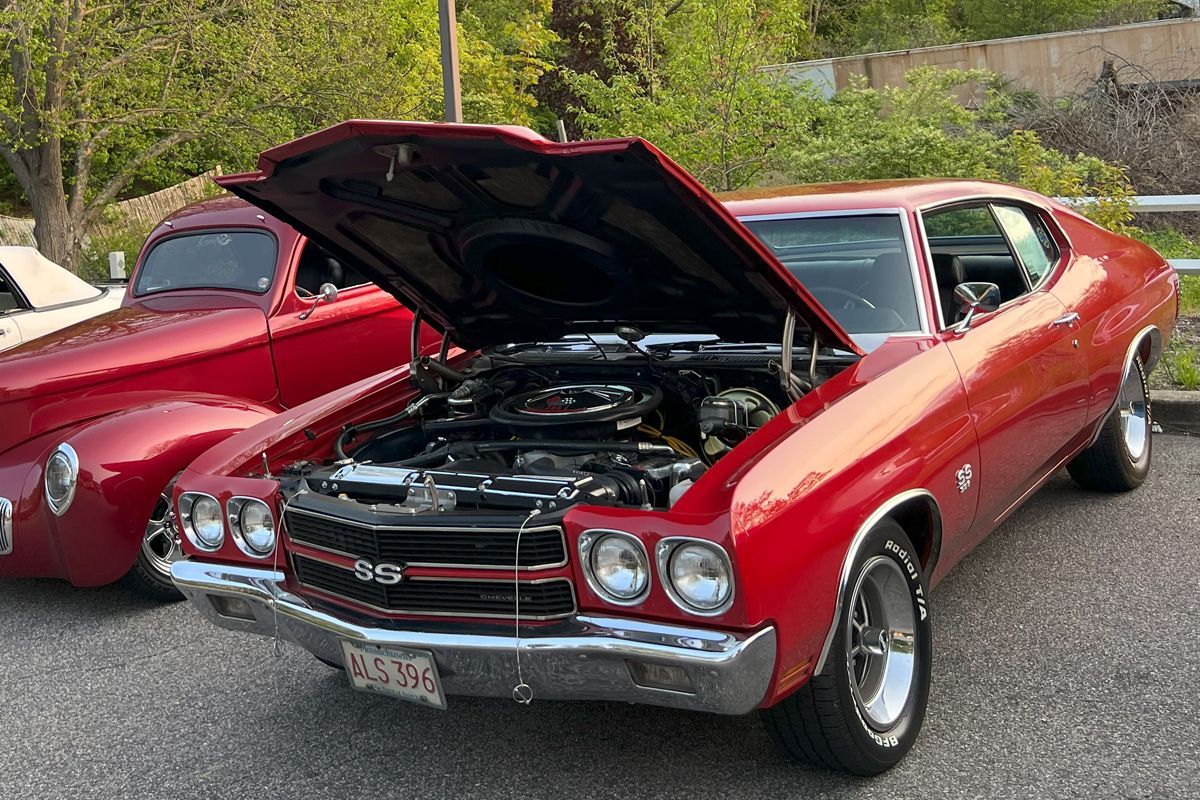 A red car with the hood up is parked next to another red car.