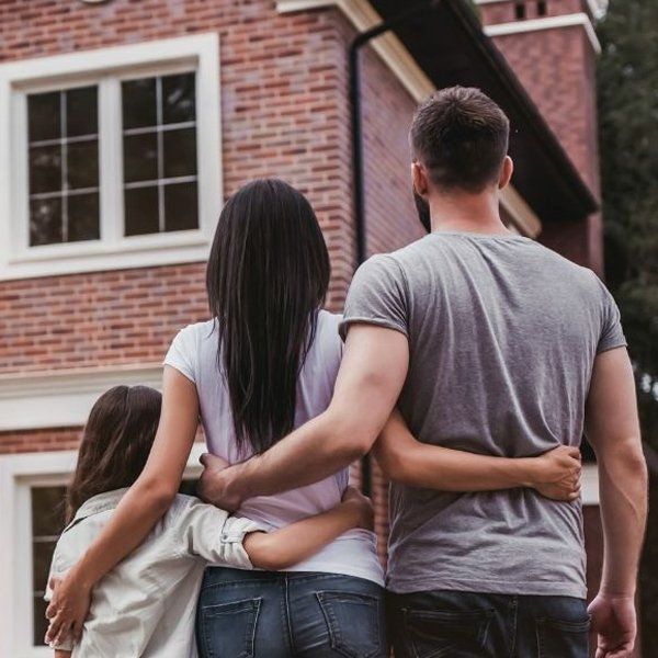 A man and two women are standing in front of a brick house