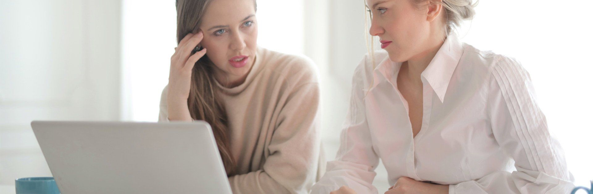 Two women are sitting at a table looking at a laptop computer.