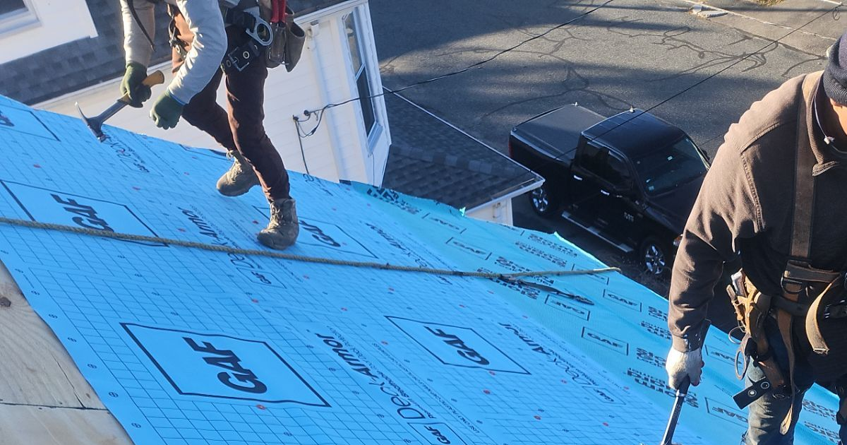 Overhead view of multiple gray shingled roof sections, some with wooden truss supports.