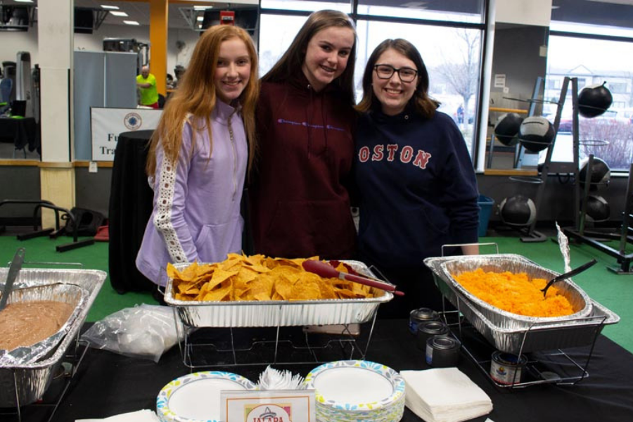 Three girls are posing for a picture in front of a table with food.