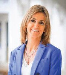 A woman in a blue jacket and necklace is smiling for the camera.