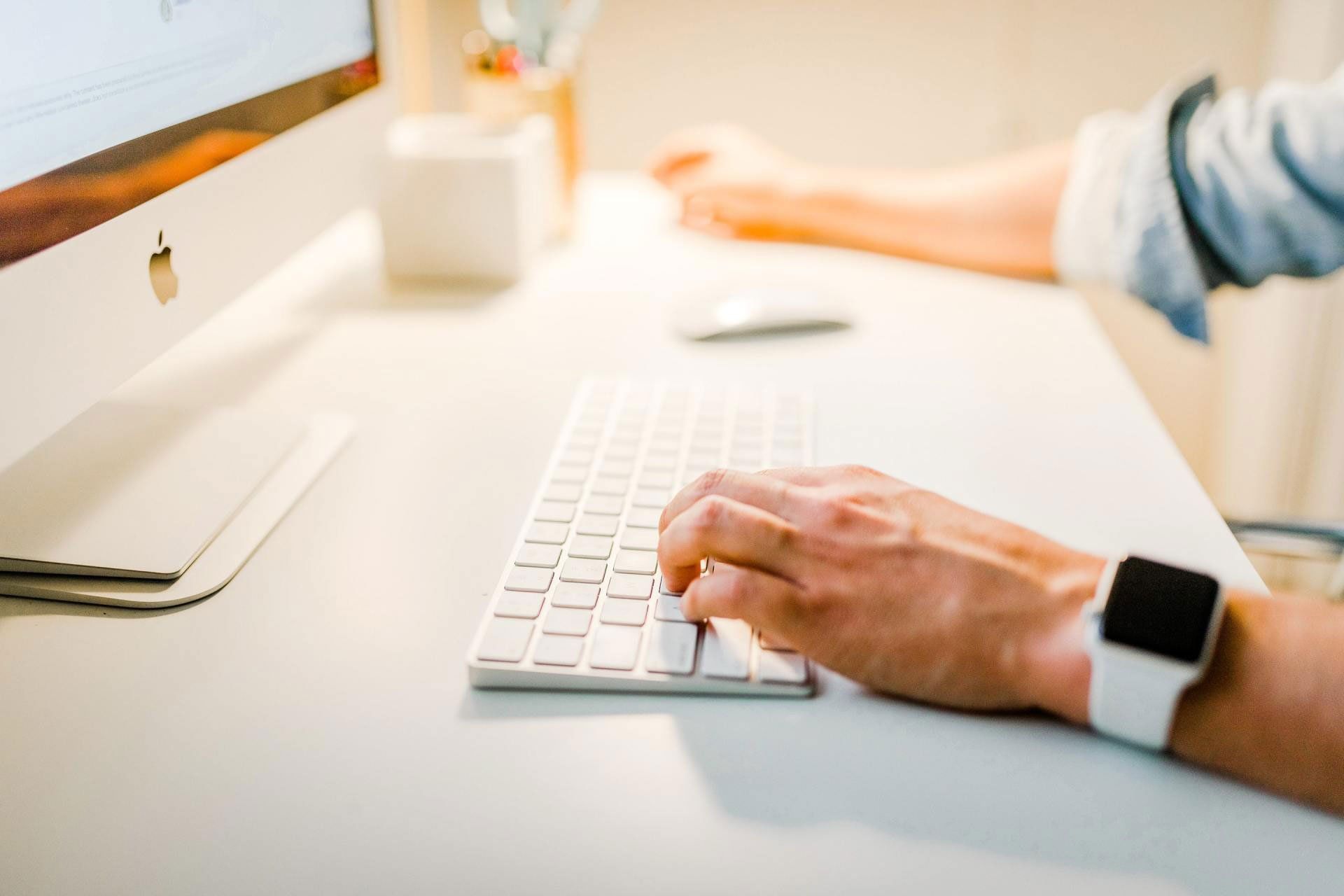 A person wearing an apple watch is typing on a computer keyboard.