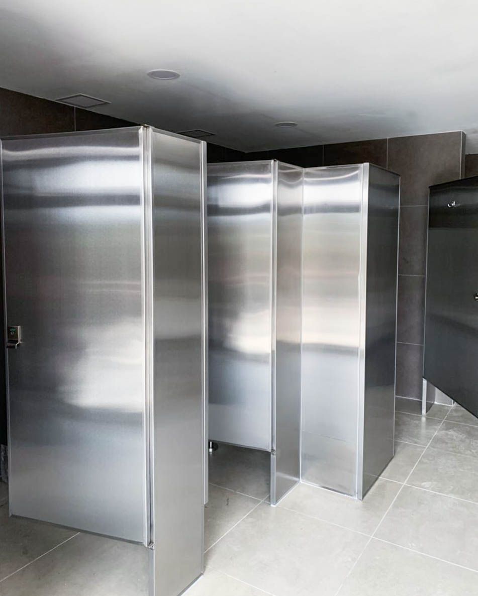 Una fila de cubículos sanitarios de acero inoxidable en un baño público.