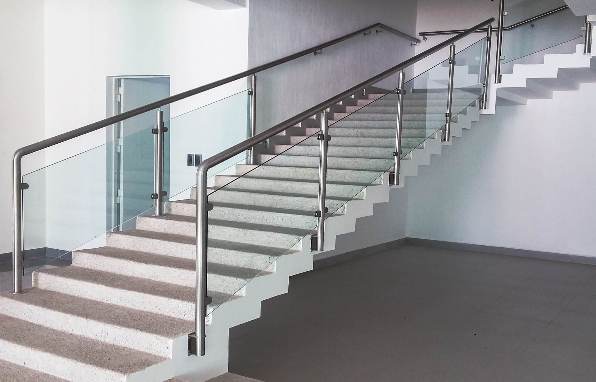 Una escalera vacía con barandilla de cristal en un edificio.