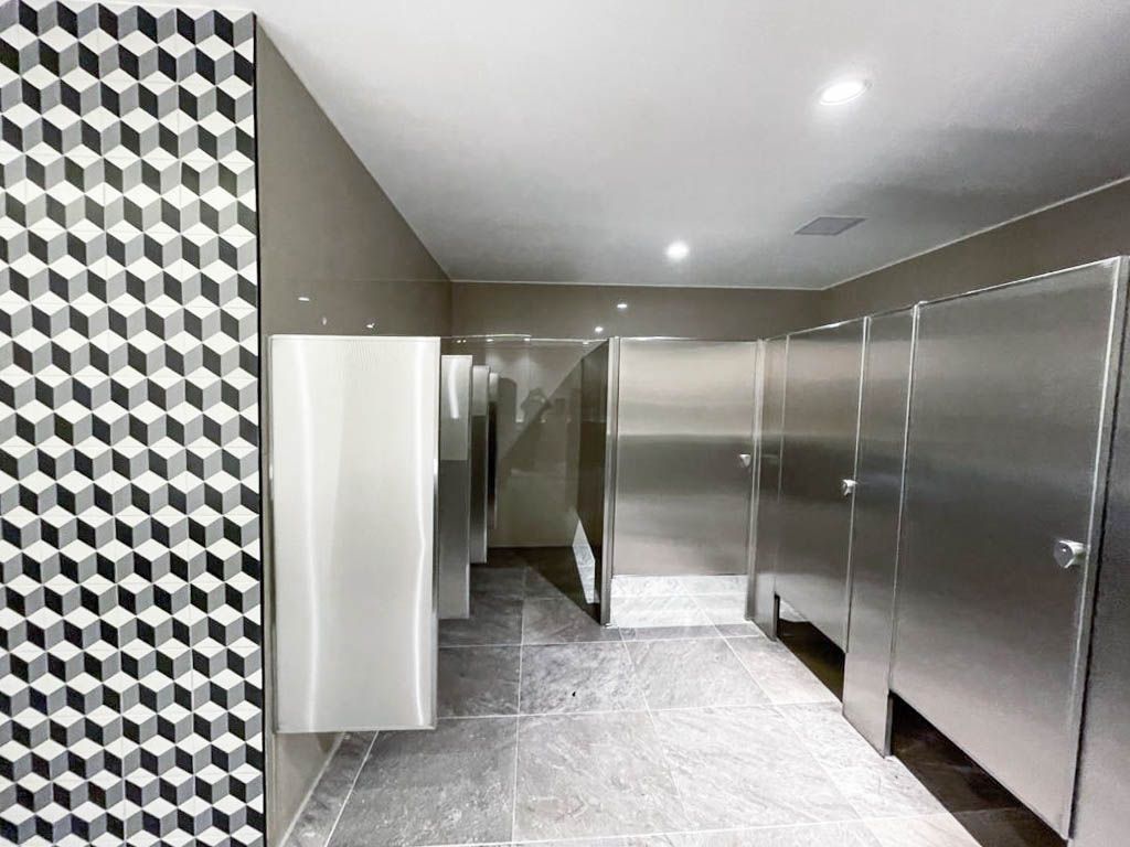 Un baño público con cubículos y cubículos de acero inoxidable.