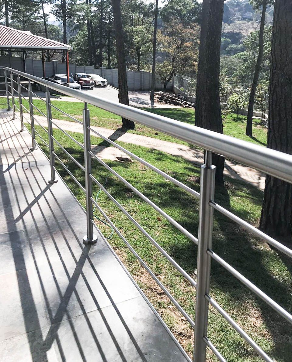 Una barandilla de acero inoxidable está rodeada de césped y árboles.