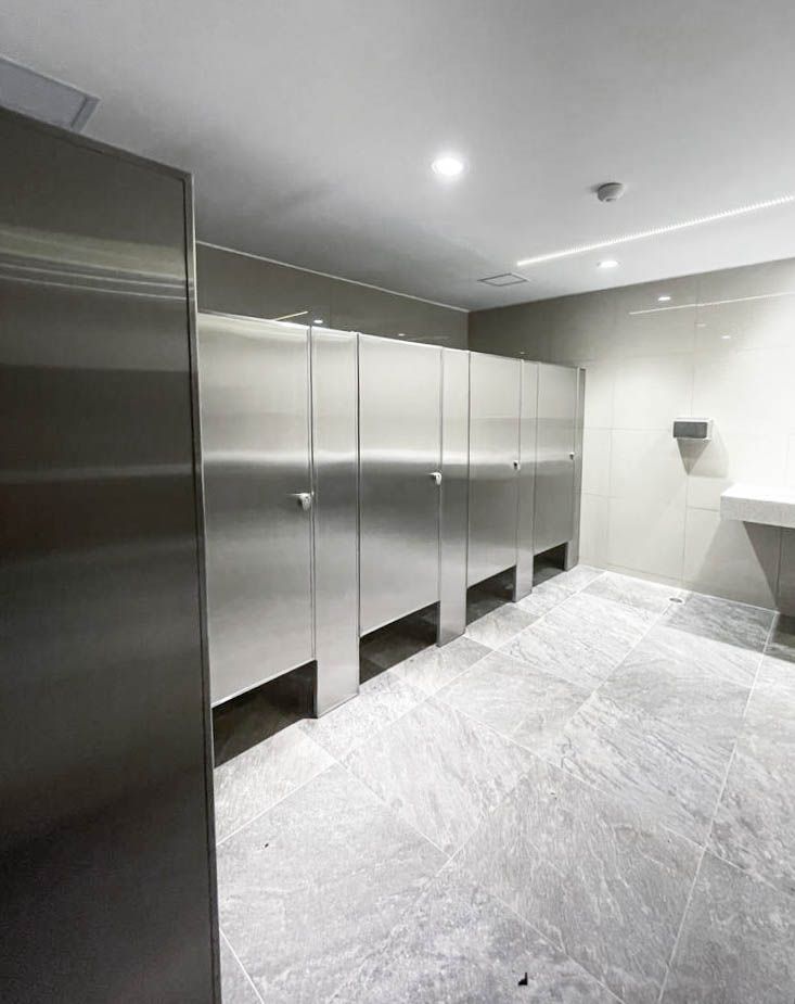 Un baño público con cubículos de acero inoxidable y lavabo.