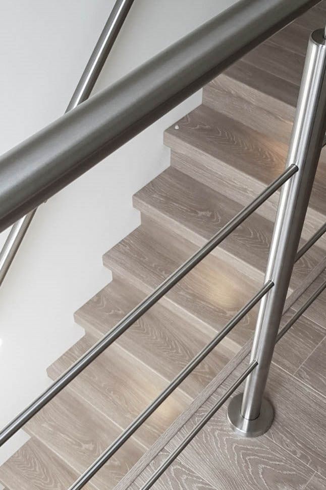 Un primer plano de una escalera de madera con barandilla de acero inoxidable.