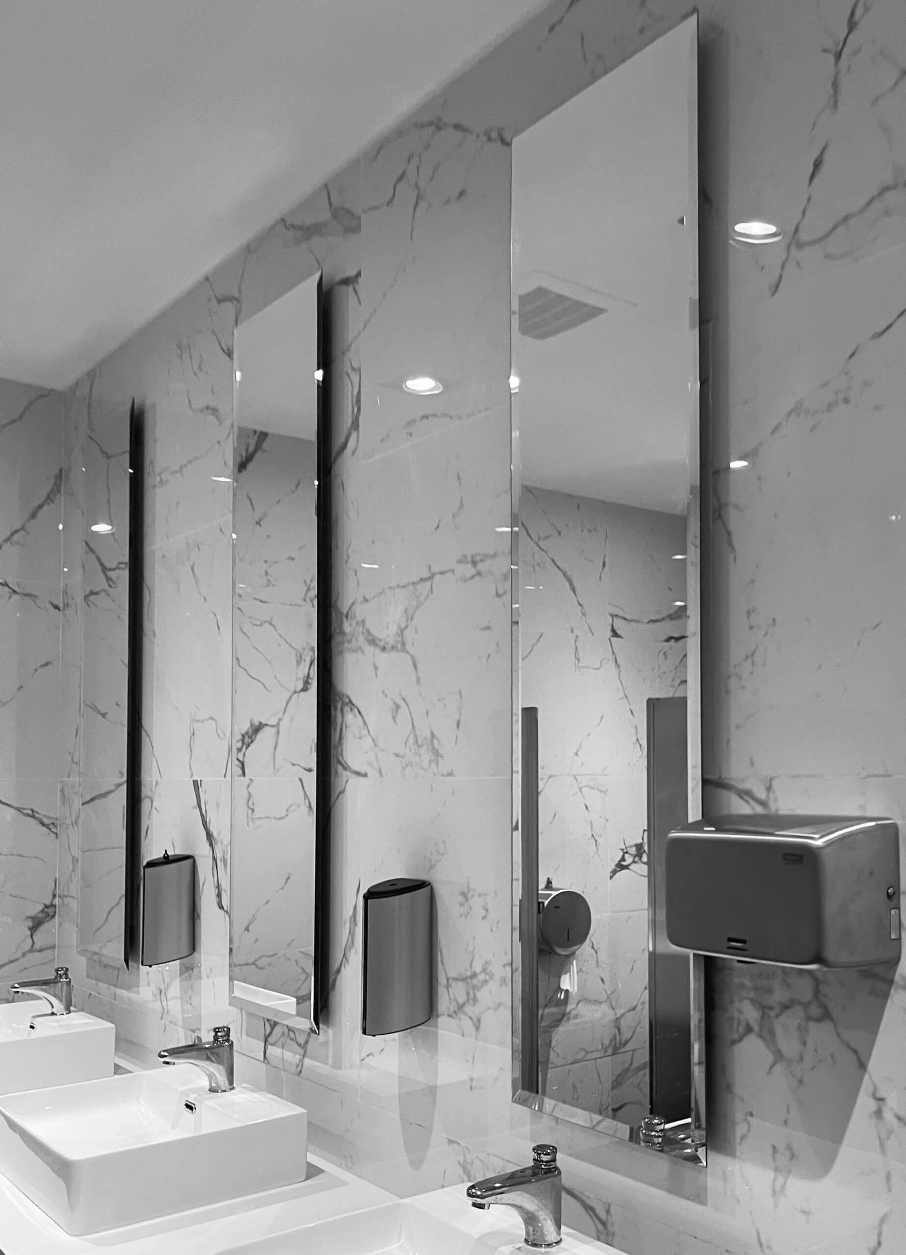 Una fotografía en blanco y negro de un baño con dos lavabos y tres espejos.
