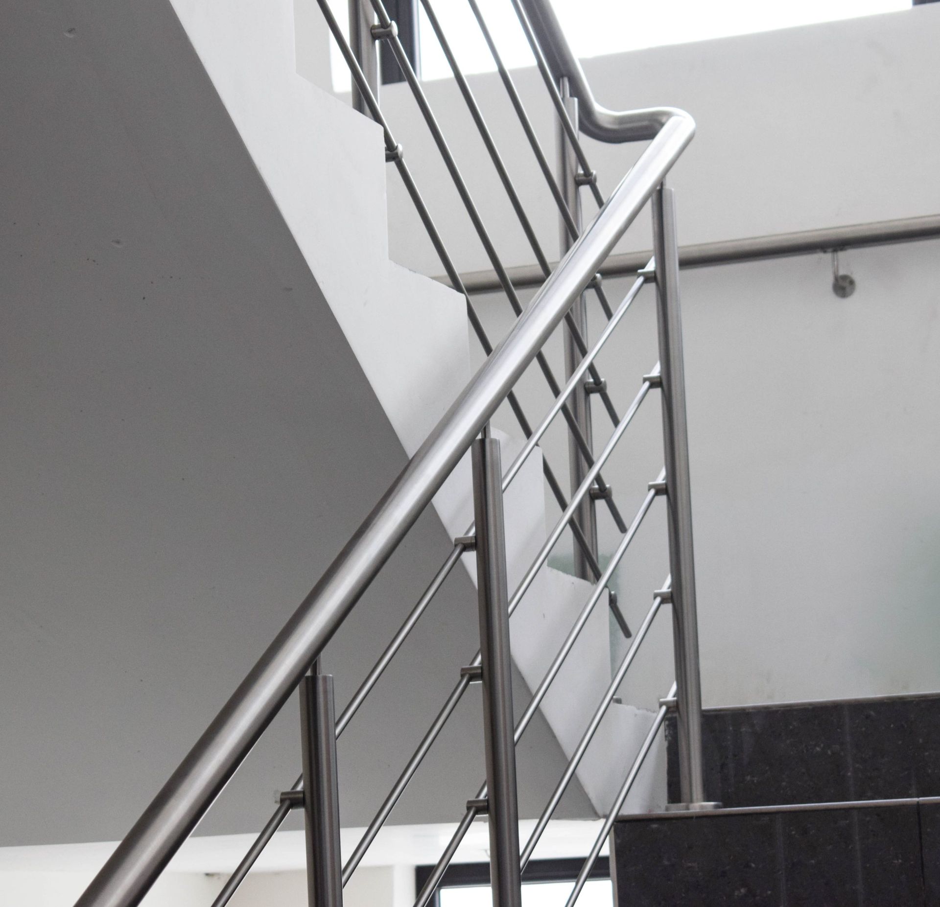 Una escalera con barandilla de acero inoxidable y escalones negros.