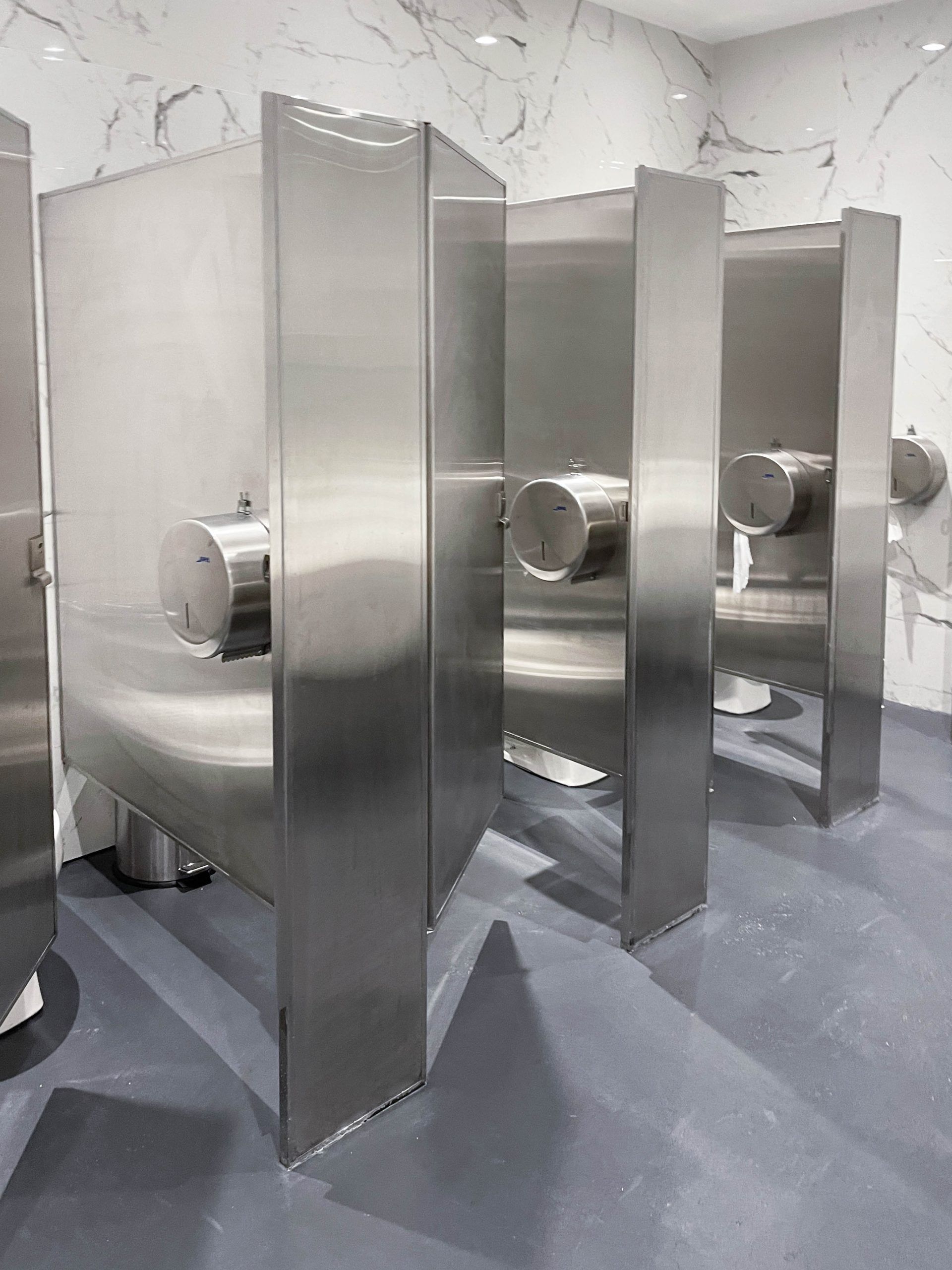 Una fila de cubículos sanitarios de acero inoxidable en un baño público.