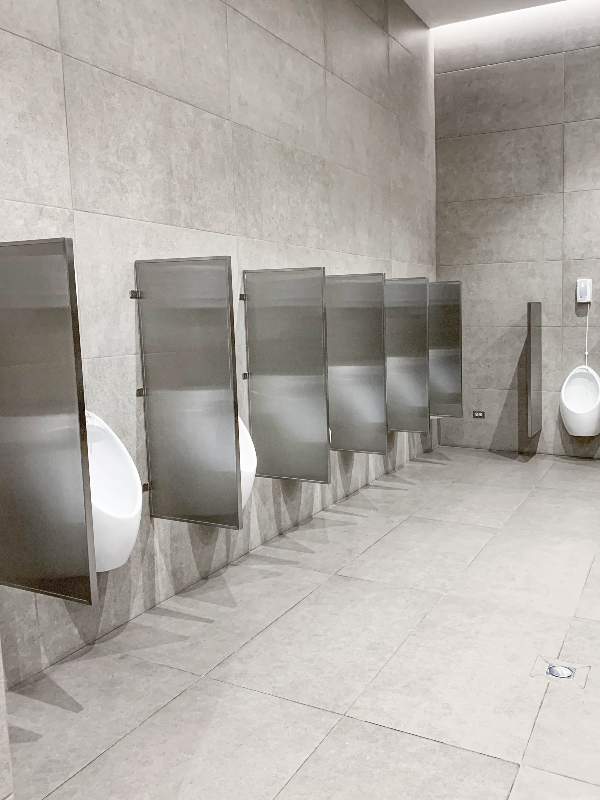 Una fila de urinarios en un baño público con divisores de acero inoxidable