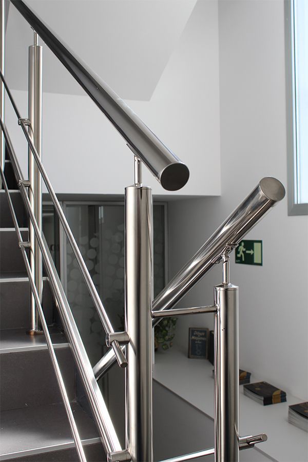 Una escalera con barandilla de acero inoxidable y una señal de salida verde.