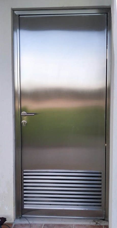 Una puerta de acero inoxidable con una rejilla de ventilación en un lateral.