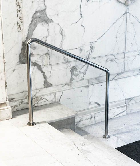 Una escalera con barandilla de metal y una pared de mármol