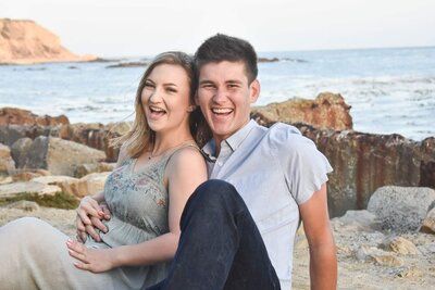 A man and a woman are sitting next to each other on a rocky beach.