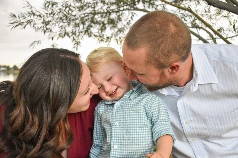 Family, mother and father kissing a child on both sides. Child smiles.