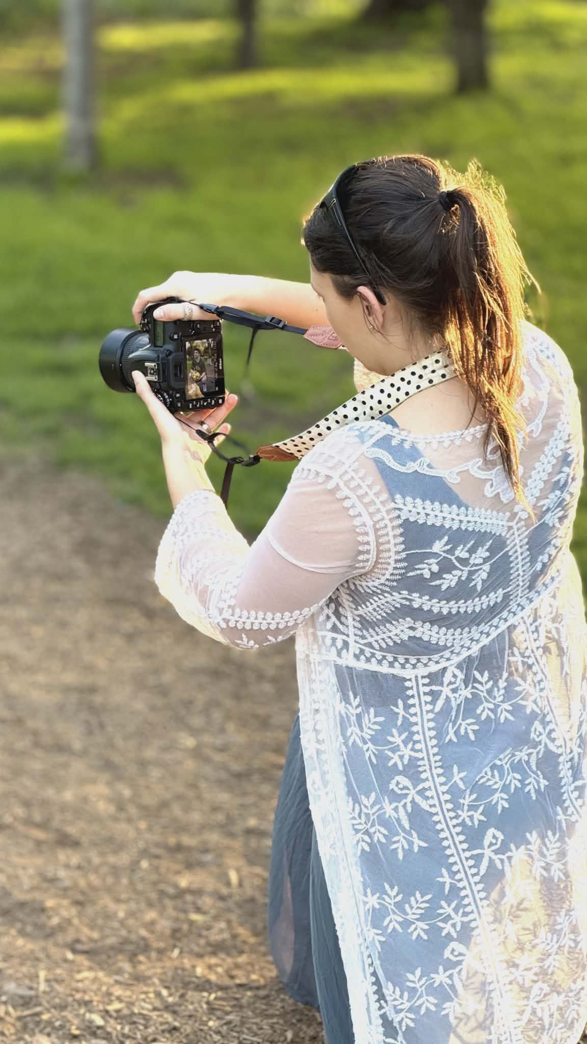 Woman holding camera, outdoors by wooden fence, focused on taking photo.