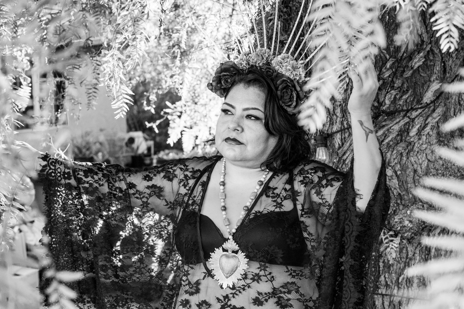 A black and white photo of a woman in a lace top and crown standing in the woods.