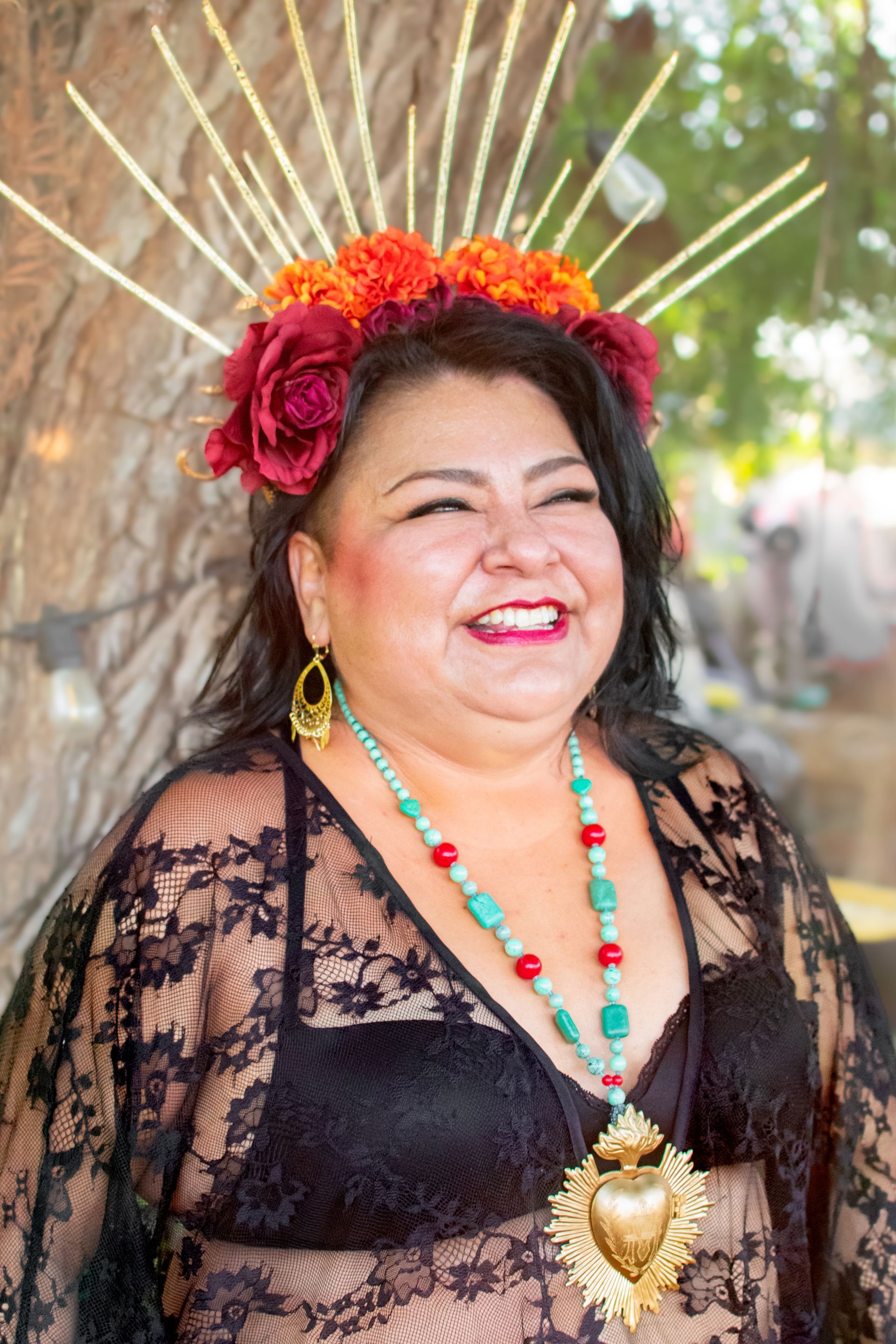 A woman wearing a crown of flowers and a necklace is smiling.