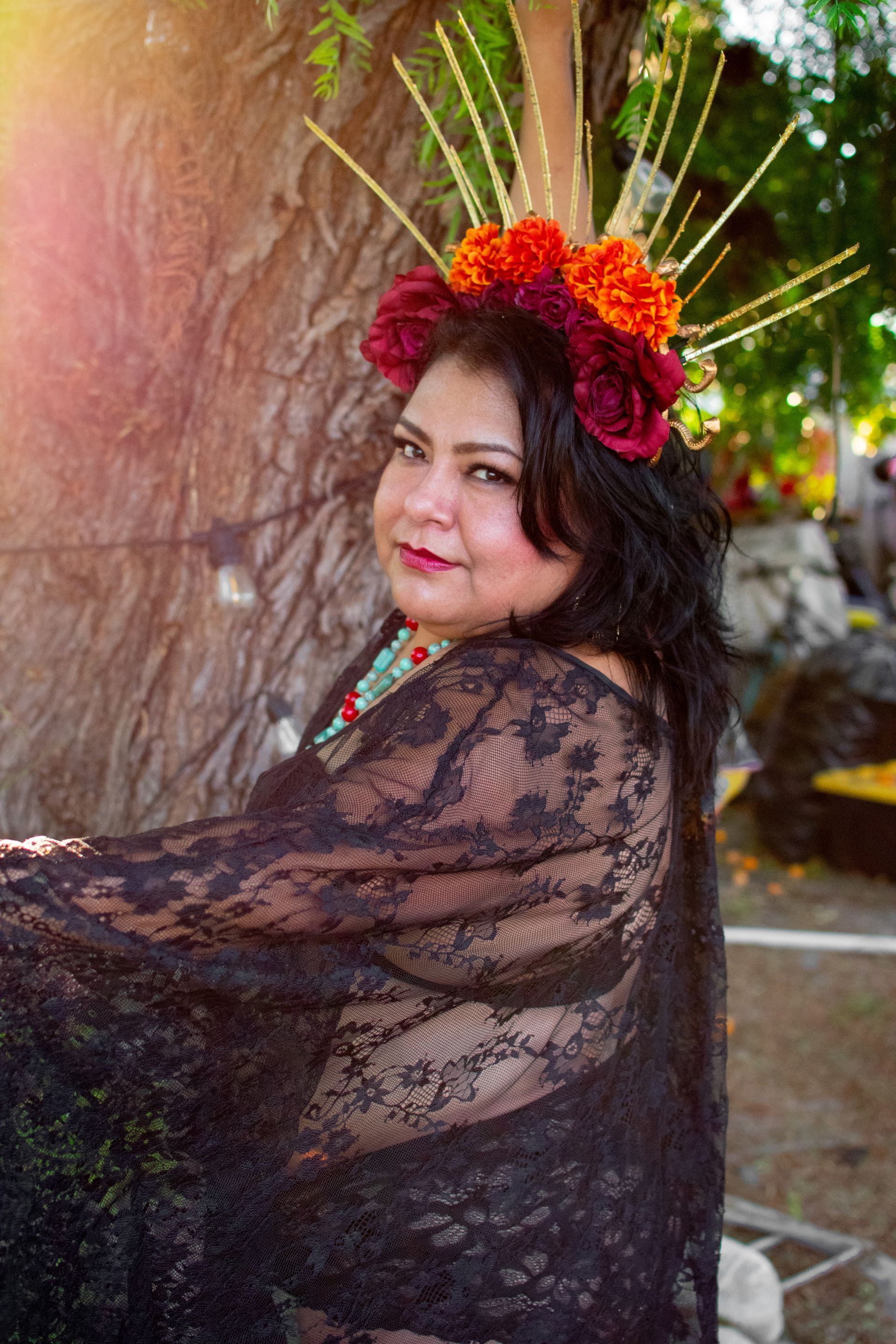 A woman wearing a flower crown is sitting next to a tree.