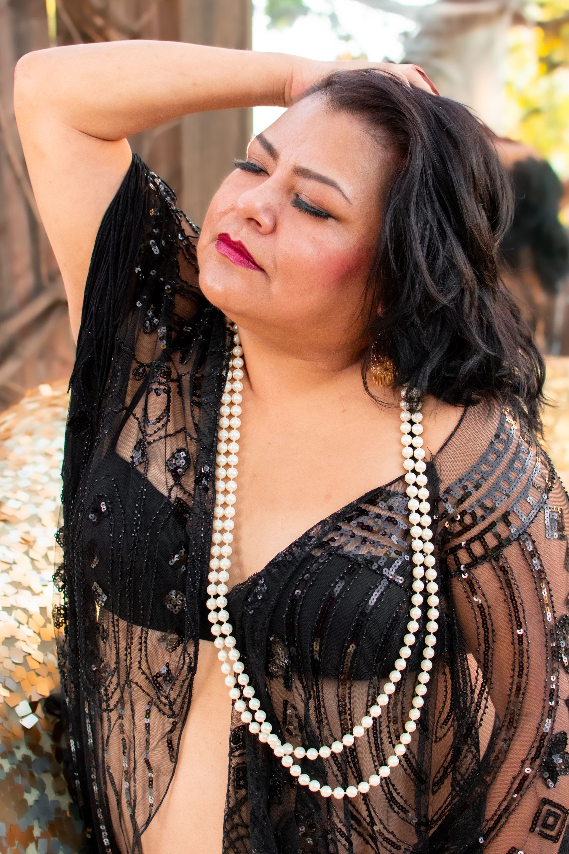 A woman is wearing a black top and a pearl necklace.