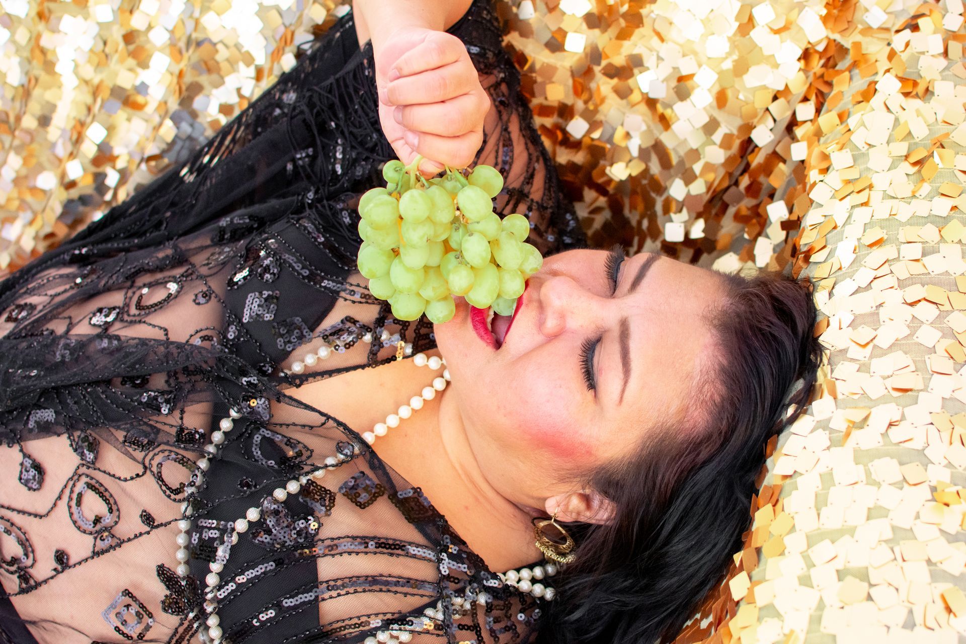 A woman is seductively eating grapes while lying on her back.