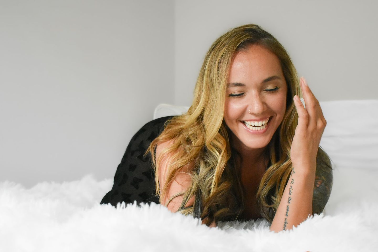 Woman lying on bed, smiling, with long wavy blonde hair.