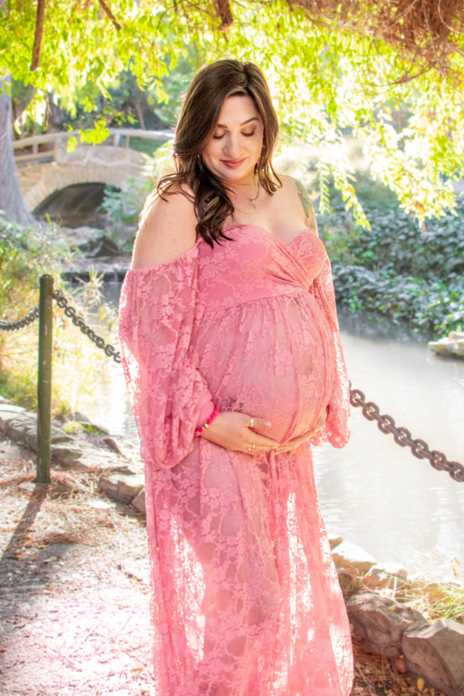 A pregnant woman in a pink lace dress is holding her belly. Maternity