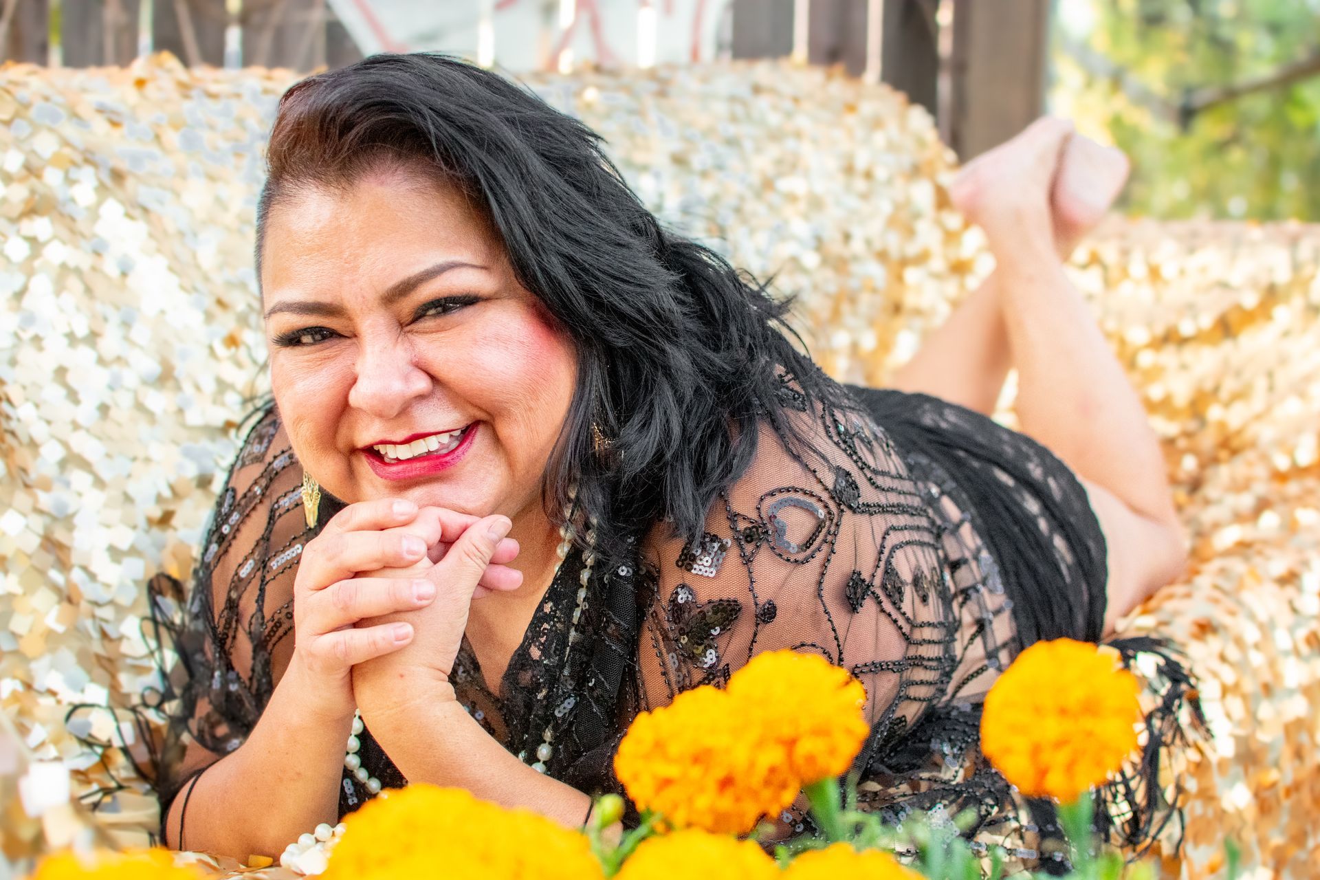 A woman is laying on her stomach on a gold couch surrounded by yellow flowers. Boudoir