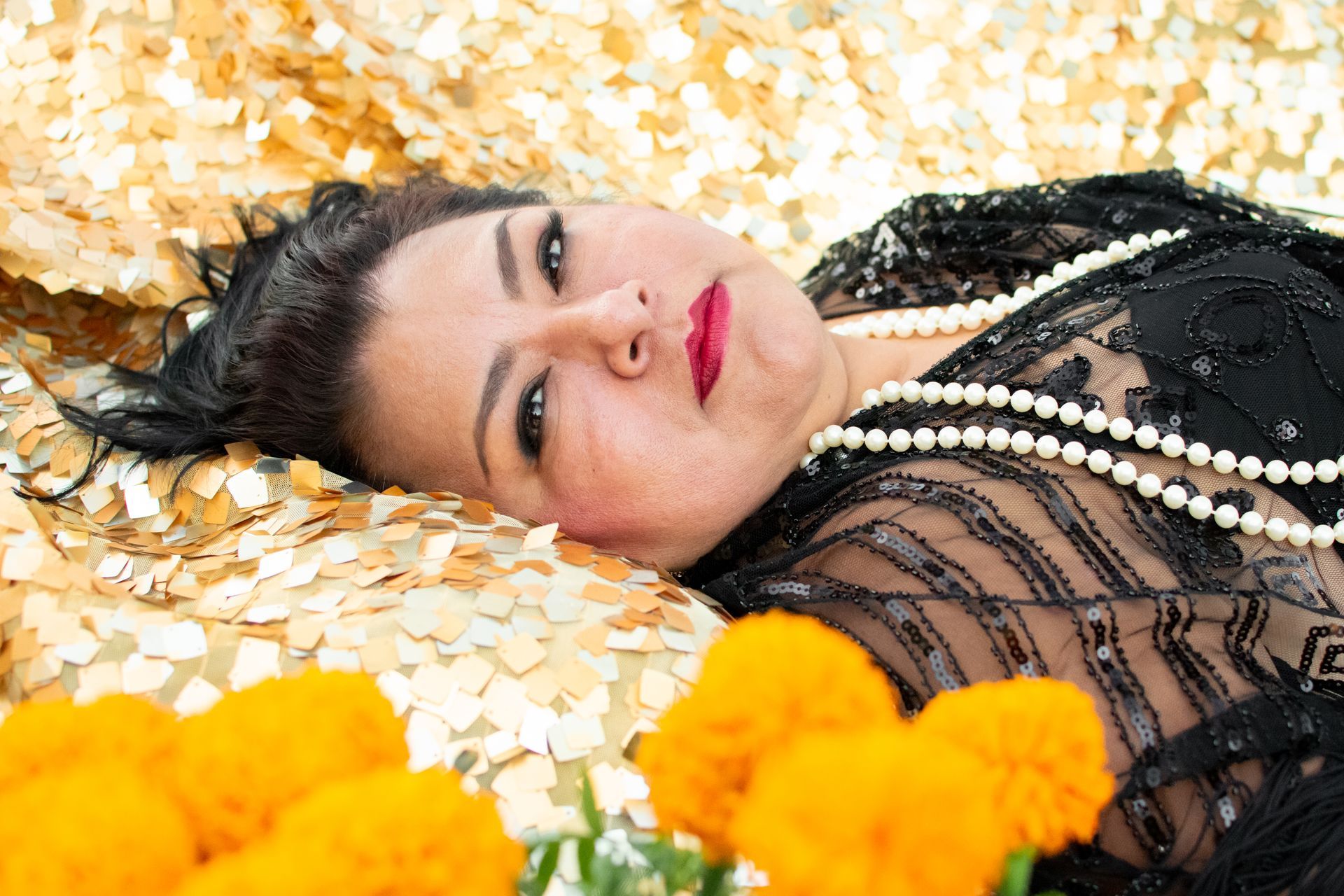 A woman in a black dress and pearls is laying on a bed.