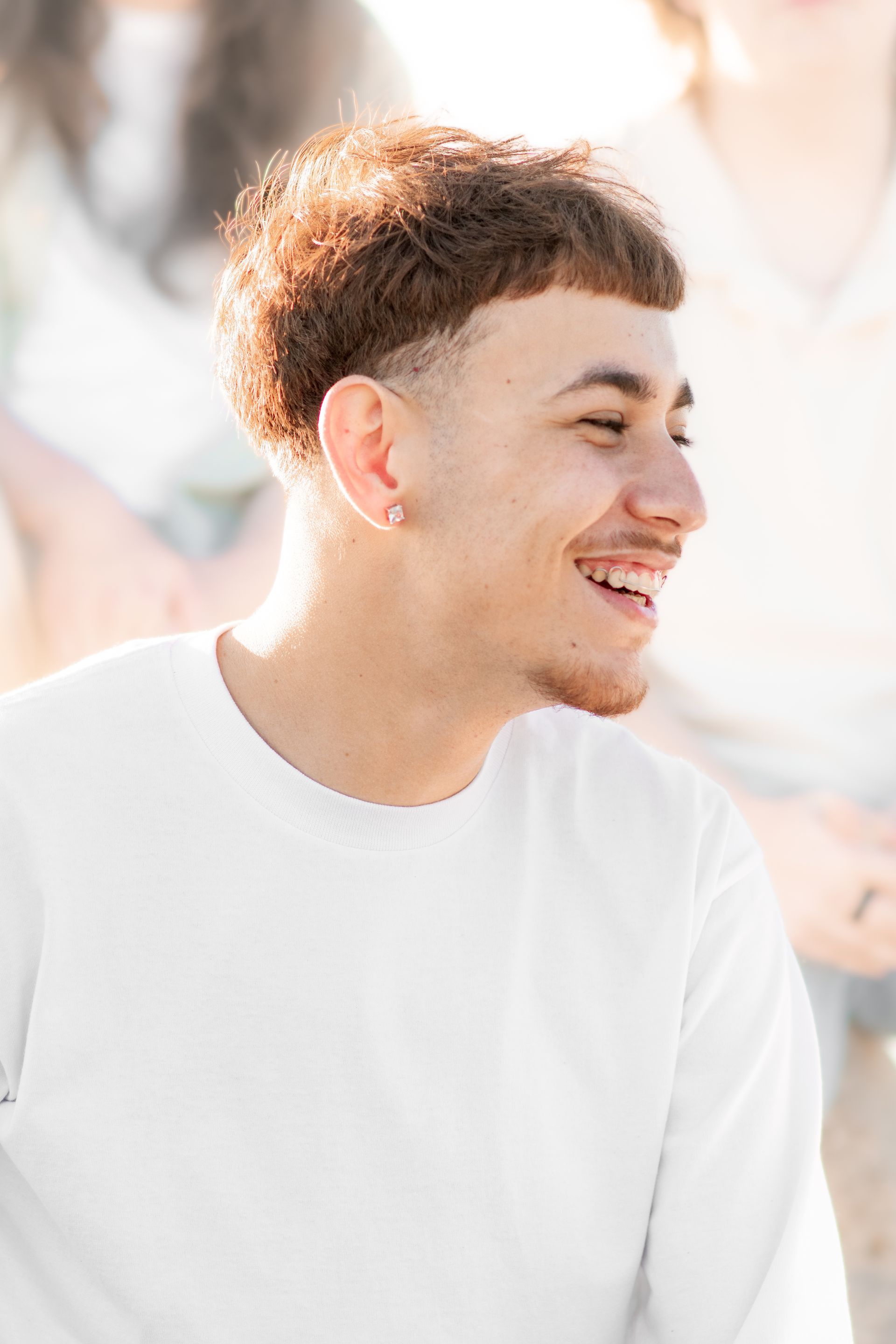 A young man in a white shirt is smiling and looking to the side at El Porto Beach.