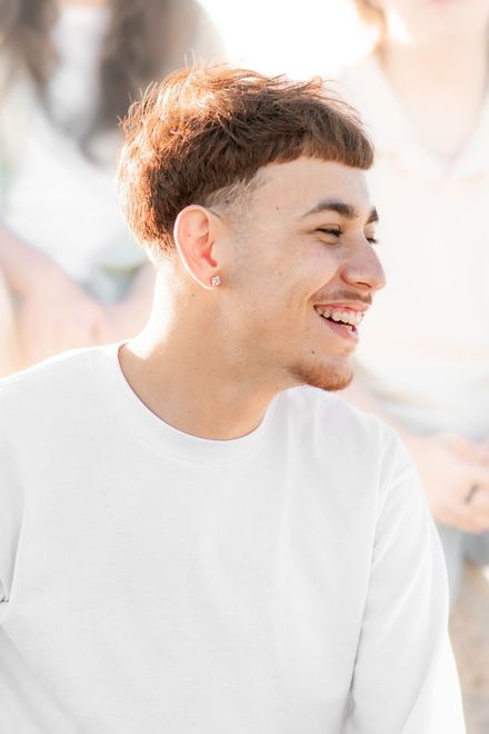 Smiling person with short, brown hair and a clean haircut, wearing a white long-sleeve shirt.