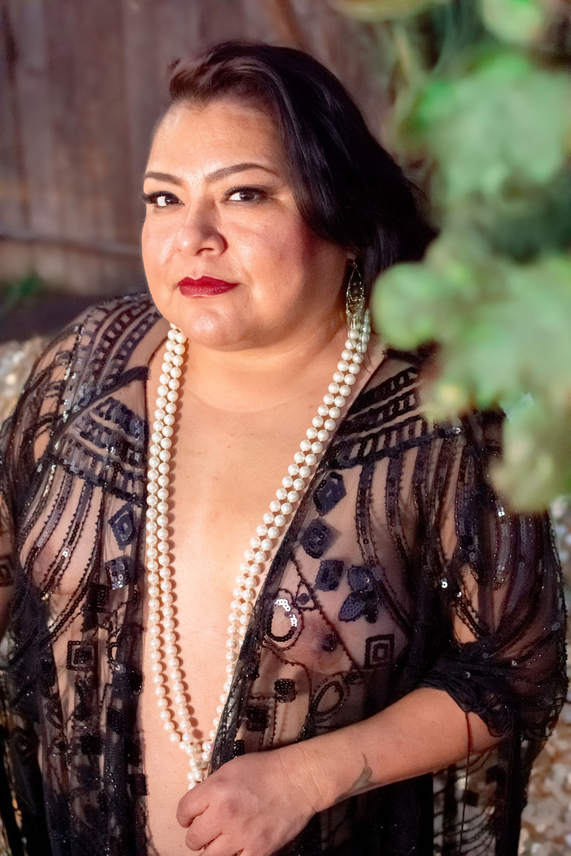 A woman is wearing a pearl necklace and a sheer top.